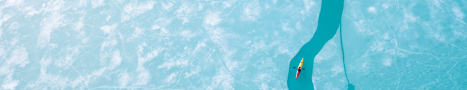 Aerial view of a person kayaking through turquoise-colored water amid sheets of ice (source: Getty Images)